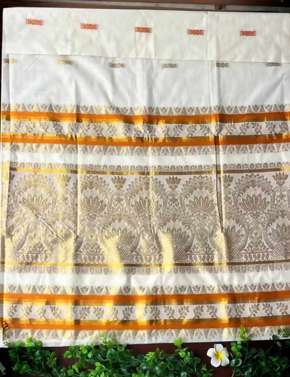 House Of Paramya off-white cotton Kasavu saree featuring golden lotus jacquard patterns and a vibrant orange border.