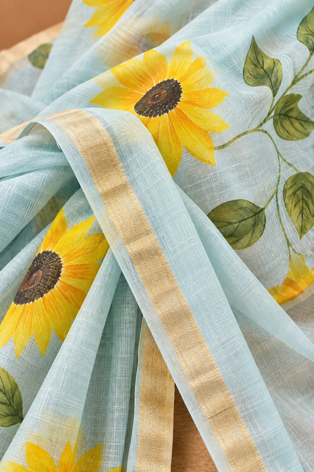 House Of Paramya powder blue linen cotton saree with vibrant sunflower prints and a delicate gold zari border.