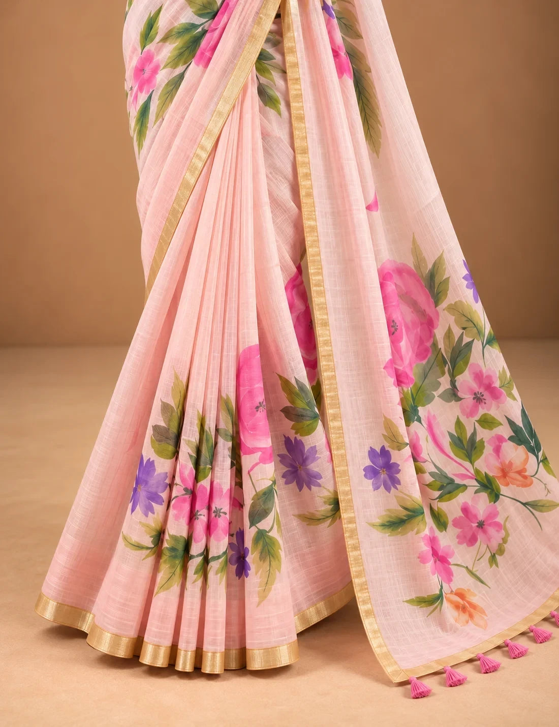 House Of Paramya blush pink linen saree with watercolor floral prints, gold border, and decorative tassel pallu.