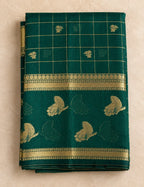 House Of Paramya bottle green raw silk saree featuring a gold checkered pattern, floral butis, and zari vine border.