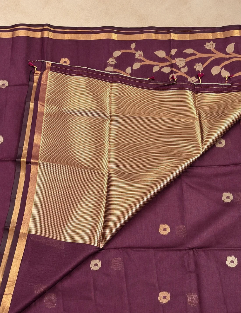 House Of Paramya plum raw tussar cotton saree featuring gold zari floral pallu, zari buttis, and a striped blouse piece