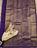 House Of Paramya dark purple Kanchipuram silk saree with intricate silver zari weaving and a decorative floral accent.