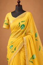 House Of Paramya yellow pure linen saree with green leaf motifs and a subtle gold-toned woven border on a mannequin.